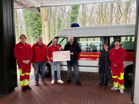 Gruppe von Personen mit Scheck vor Einsatzfahrzeug